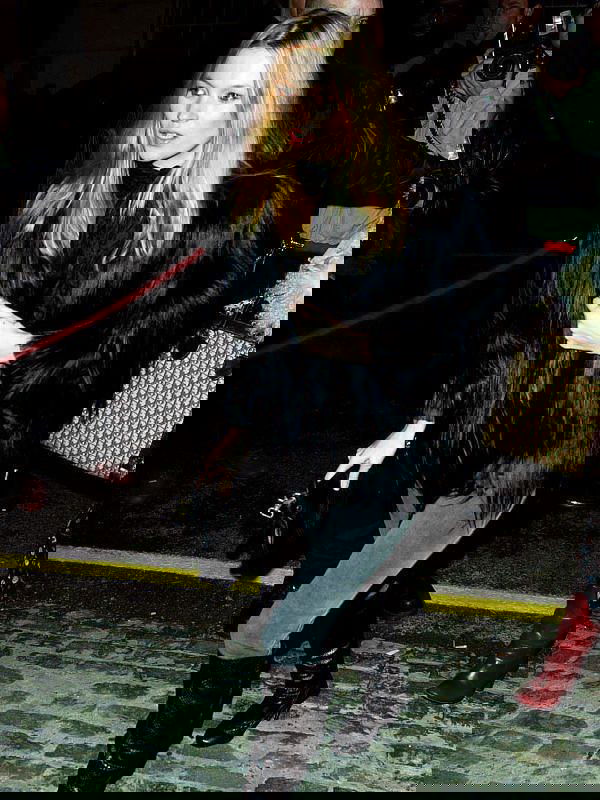 Чёрная объёмная шуба и узкие брюки на фоне ночной улицы и красной ковровой дорожки — образ для выхода в свет в холодное время года.