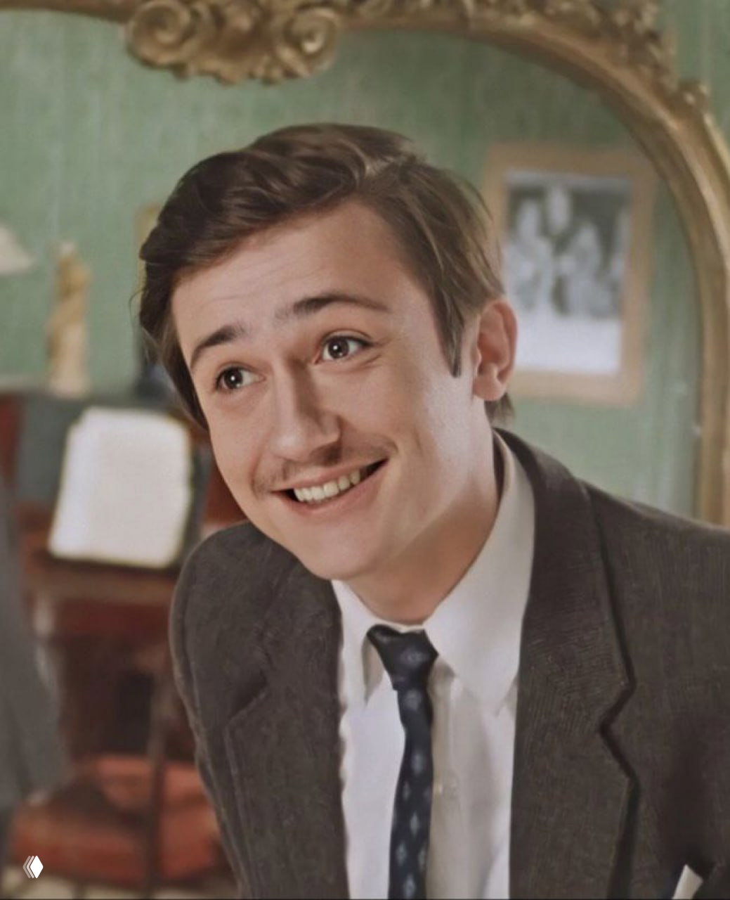 Кадр с улыбающимся молодым человеком в костюме и галстуке, тёплые тона, игровой и лёгкий характер мимики, атмосфера старой комедии.