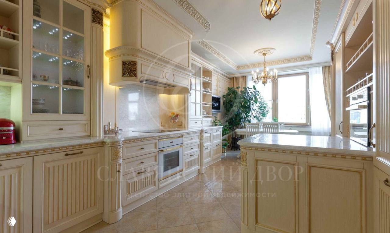 Классическая просторная кухня с островом, встроенной техникой, мраморной столешницей и панорамным окном, интерьер оформлен в светлых тонах.