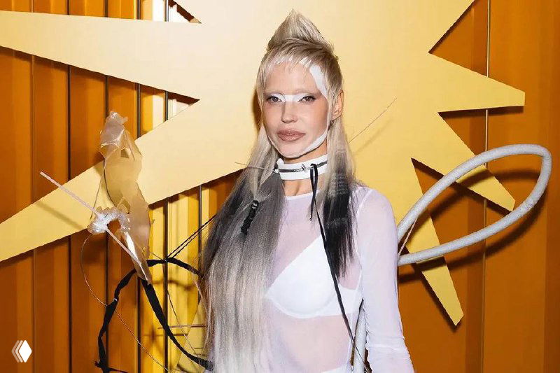 Глюкоза в авангардном белом образе с необычной причёской и сценическим макияжем на фоне декорации — дерзкий сценический имидж певицы.