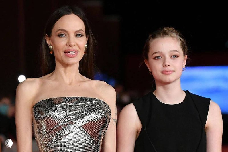 Женщина в блестящем вечернем платье рядом с молодой девушкой на красной дорожке; полуфронтальный план, фон с размытыми огнями.