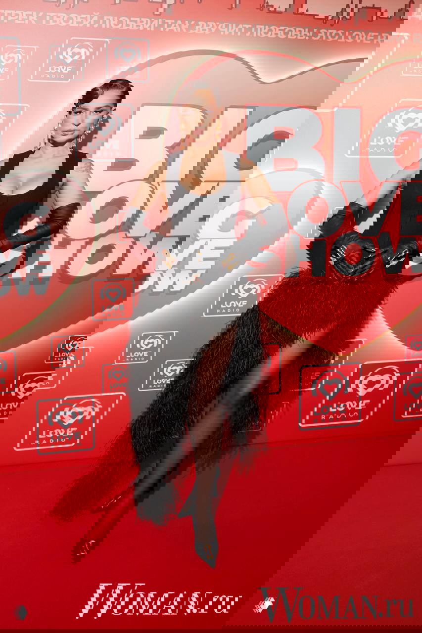 Женщина в чёрном корсете и асимметричной перьевой юбке с длинными перчатками позирует на красной дорожке Love Radio.