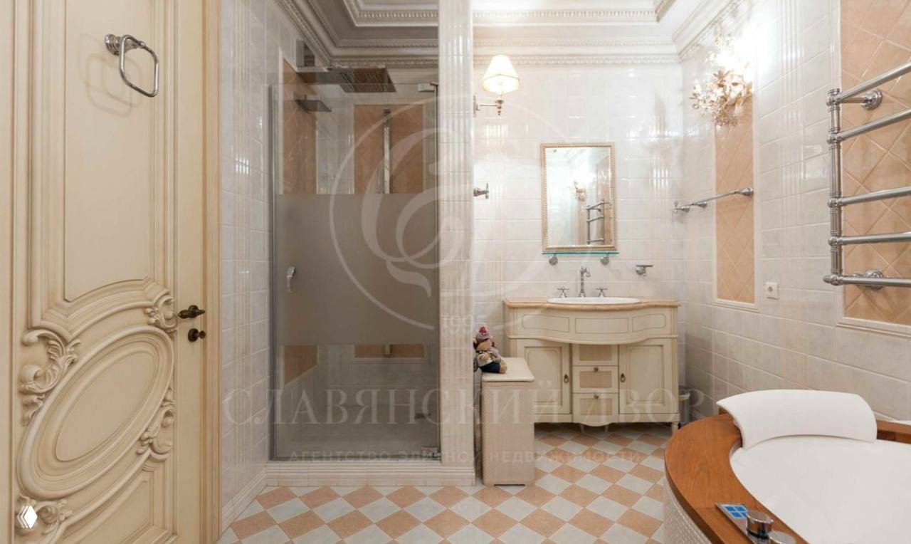 Классическая ванная комната в кремовых тонах с душевой кабиной, круглой ванной и декоративной резной дверью; плитка и фурнитура в винтажном стиле.