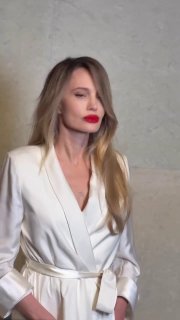 Женщина в белом пиджаке на светском мероприятии: портретный кадр в фас, длинные светлые волосы, яркая красная помада, нейтральный фон.