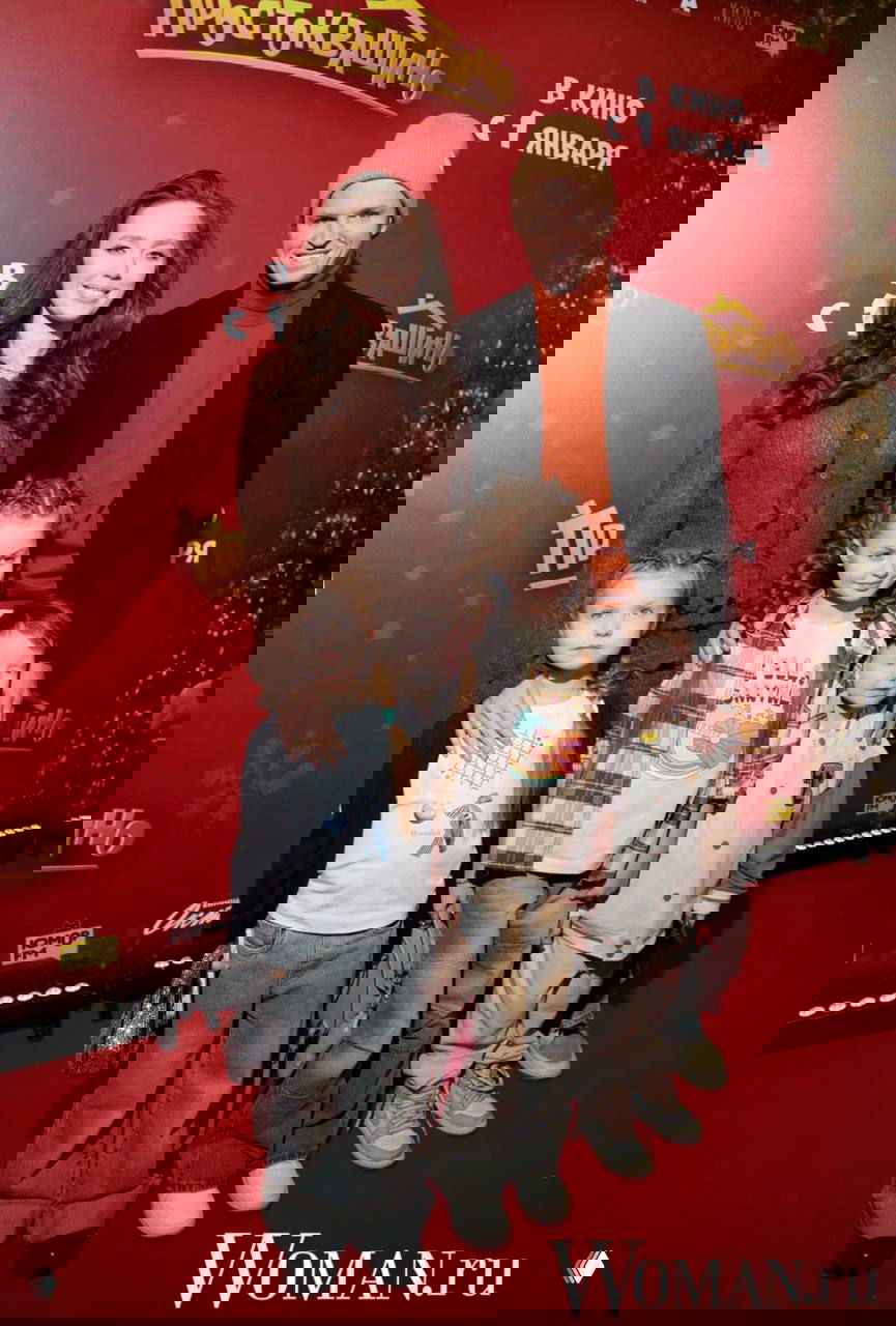 Группа знаменитостей с детьми стоит перед бренд‑стеной премьеры «Простоквашино», видны постеры и праздничная киносцена.