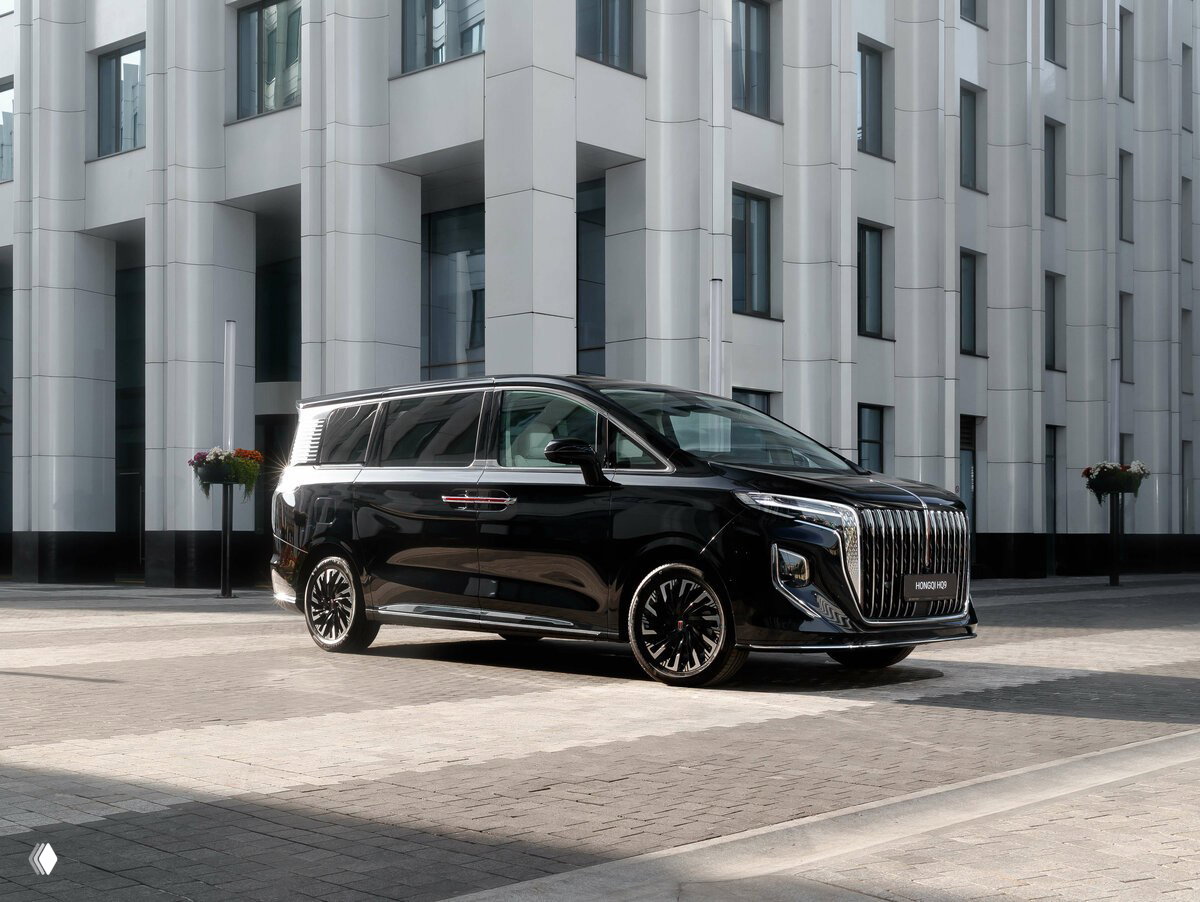 Вид сбоку на черный HONGQI HQ9 возле фасада современного здания, подчёркивающий гладкие линии и дизайн колёсных дисков.