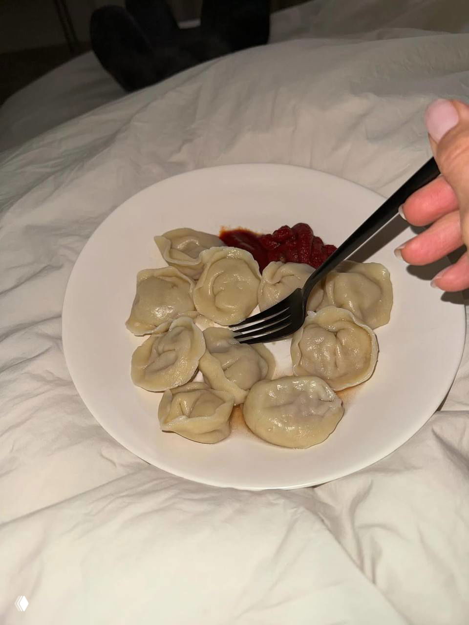 Тарелка с пельменями и кетчупом на белой посуде, крупный план на фоне постели — простой кадр домашней еды.