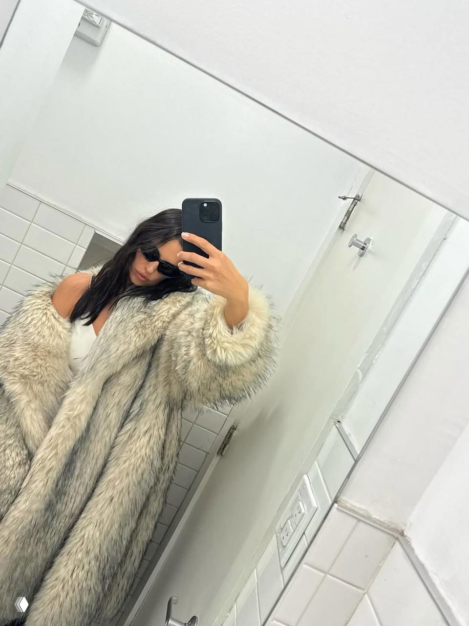 Зеркальное селфи женщины в светлой меховой шубе и тёмных очках в белой ванной комнате — модный непринуждённый образ.