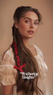 Модель с боковой косой, украшенной красной лентой, в романтическом платье; кадр из короткого ролика с надписью «Wuthering Heights».