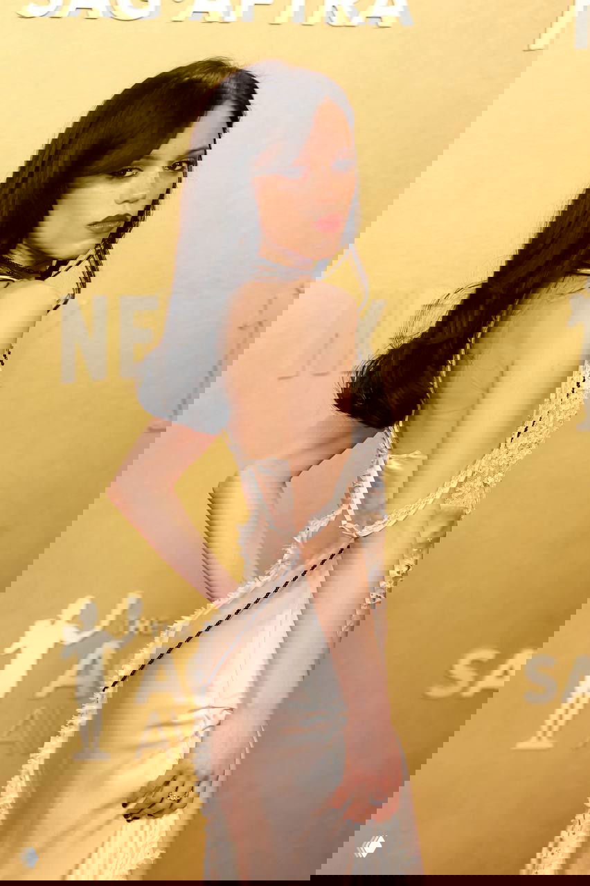 Крупный план сзади: женщина в сатиновом платье-сорочке с открытой спиной и кружевными элементами на фоне золотистой фотозоны премии.