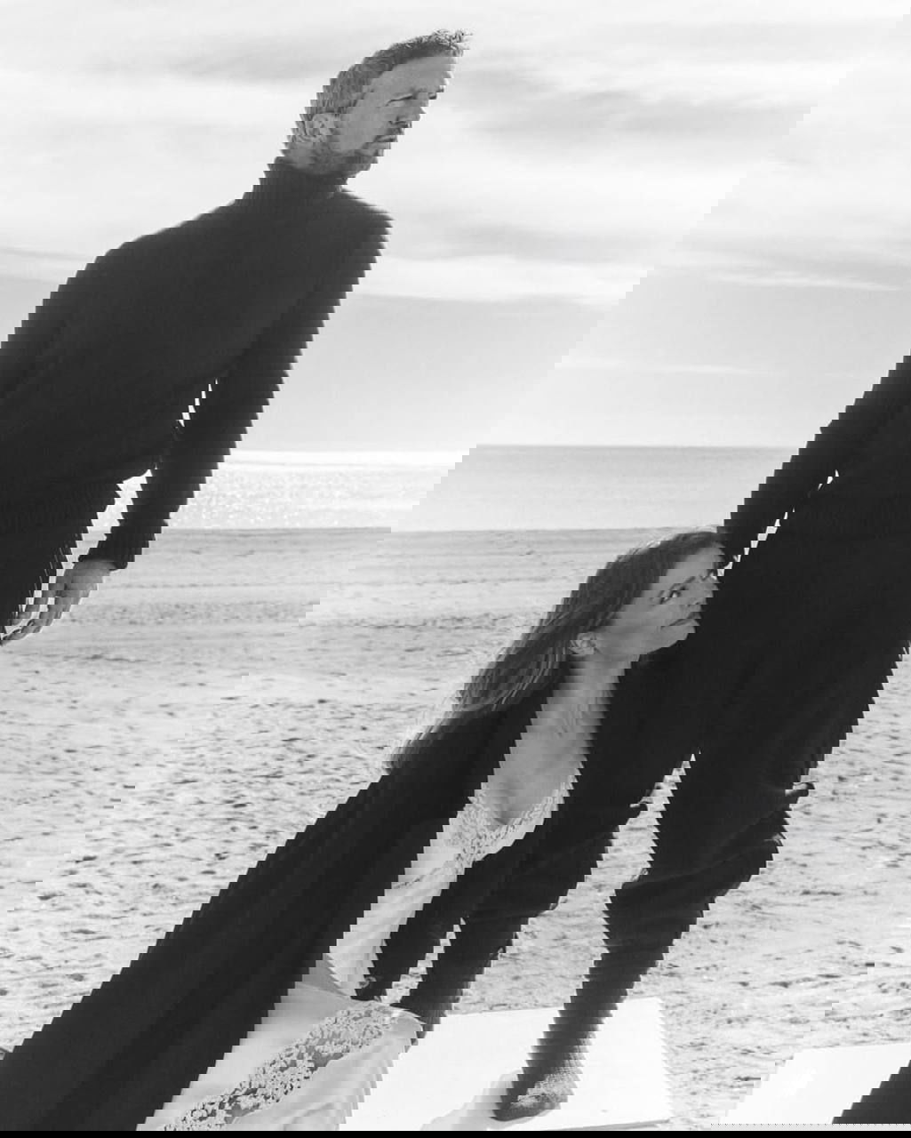 Чёрно‑белая фотокадр: мужчина и женщина в модной позе на пляже, художественная композиция и простор моря на заднем плане.