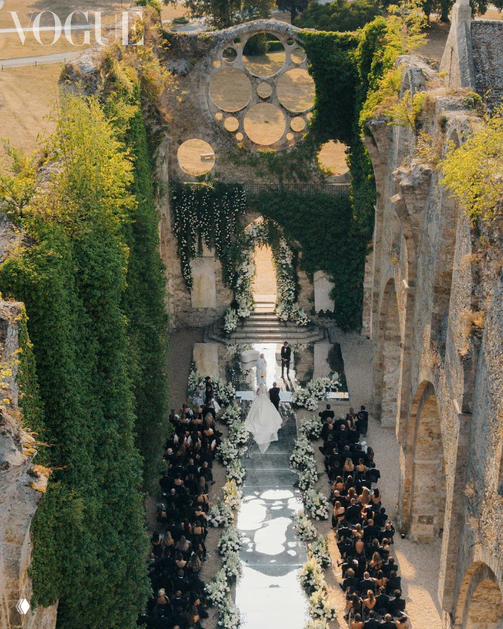 Панорамный вид на аллею церемонии в Abbaye des Vaux-de-Cernay: зеркальная дорожка, ряды гостей и флористическое оформление в белой гамме.