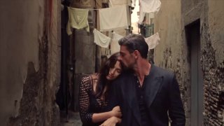 Ирина Шейк и Микеле Морроне в рекламной съёмке Dolce & Gabbana: пара в модных образах идёт по узкой улочке, атмосферный кадр.