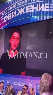 Крупный план: Ваня Дмитриенко показан на светящемся экране с логотипом премии МУЗ‑ТВ «Движение» 2026, внизу видна сцена и часть публики.