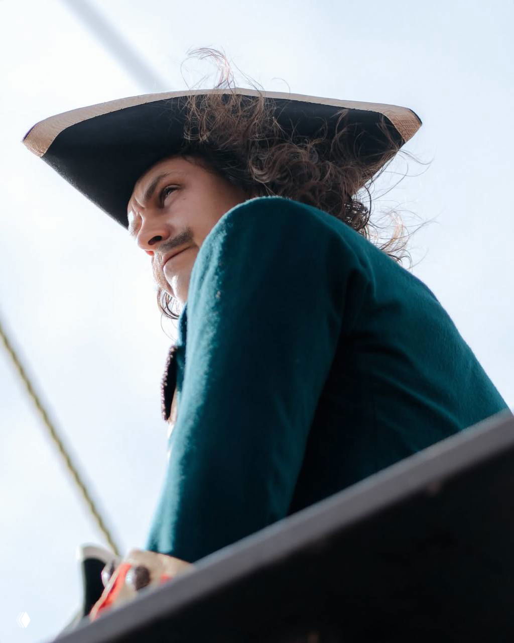 Крупный план профиля Милоша Биковича в треуголке и историческом костюме на фоне неба во время морских съемок.