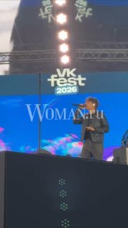 Сцена VK FEST 2026: Ваня Дмитриенко выступает перед большим экраном с логотипом фестиваля и надписью Woman.ru
