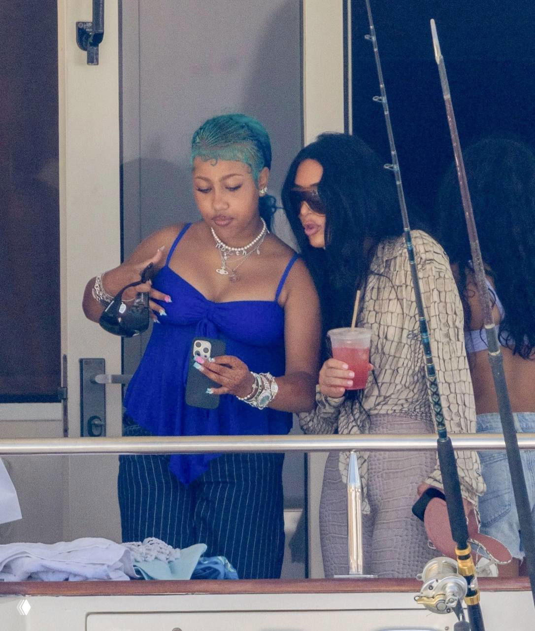 Кадр на яхте: женщина и подросток рассматривают телефон, одна держит напиток, непринуждённая атмосфера отдыха на палубе.