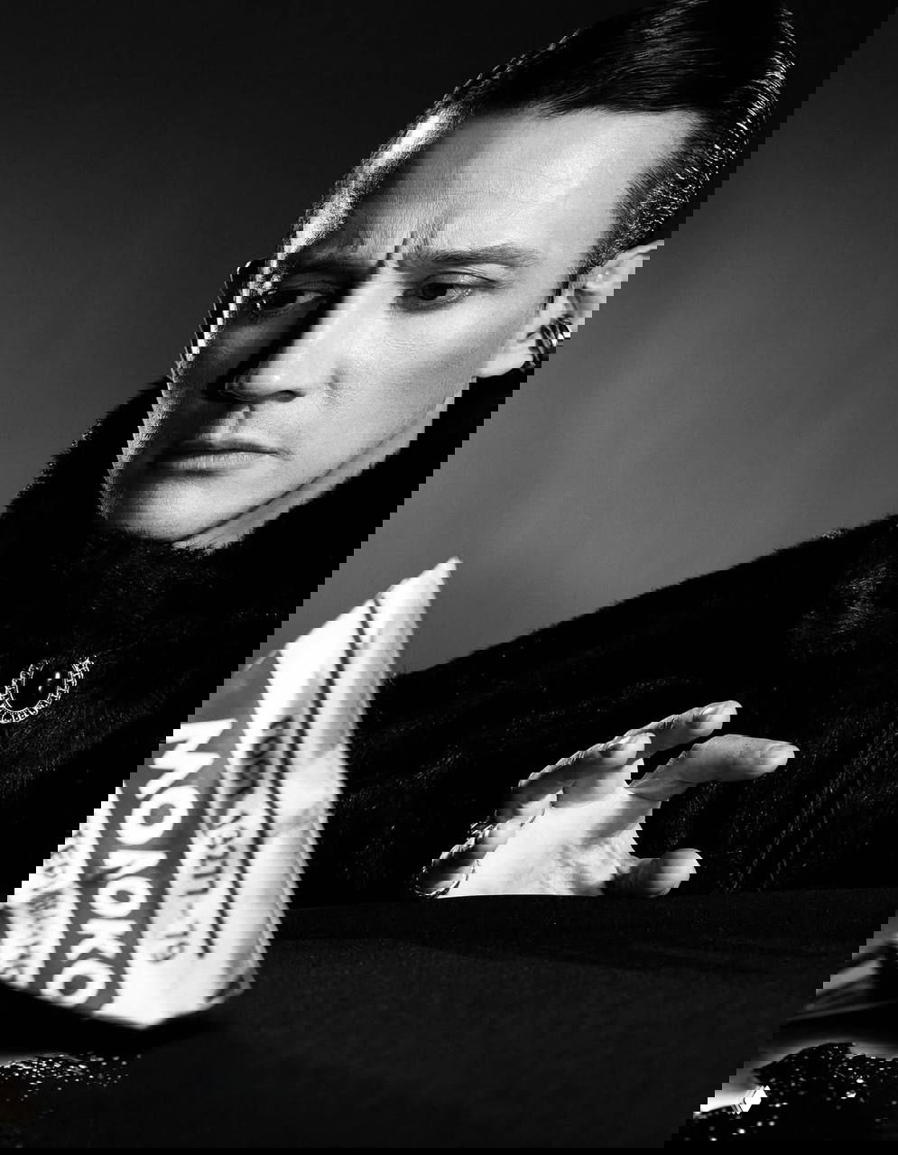 Чёрно‑белый портрет мужчины за столом с газетой «Молоко» в кадре, театральный реквизит и задумчивый взгляд в сторону, студийный свет.