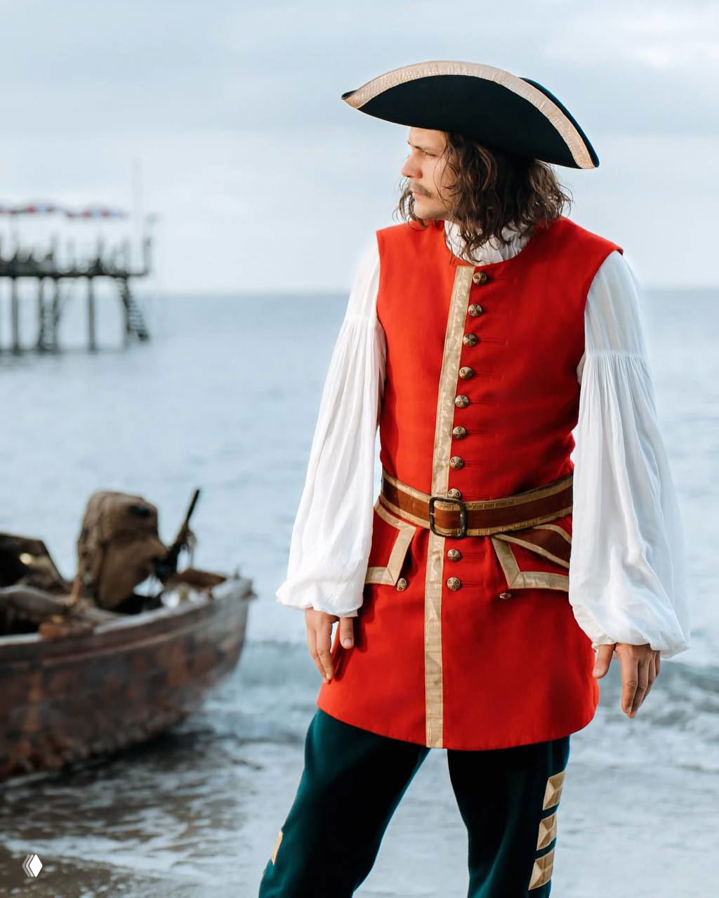 Милош Бикович в красном историческом мундире и шляпе стоит у берега рядом с лодкой — костюмированный кадр из съемочного процесса.