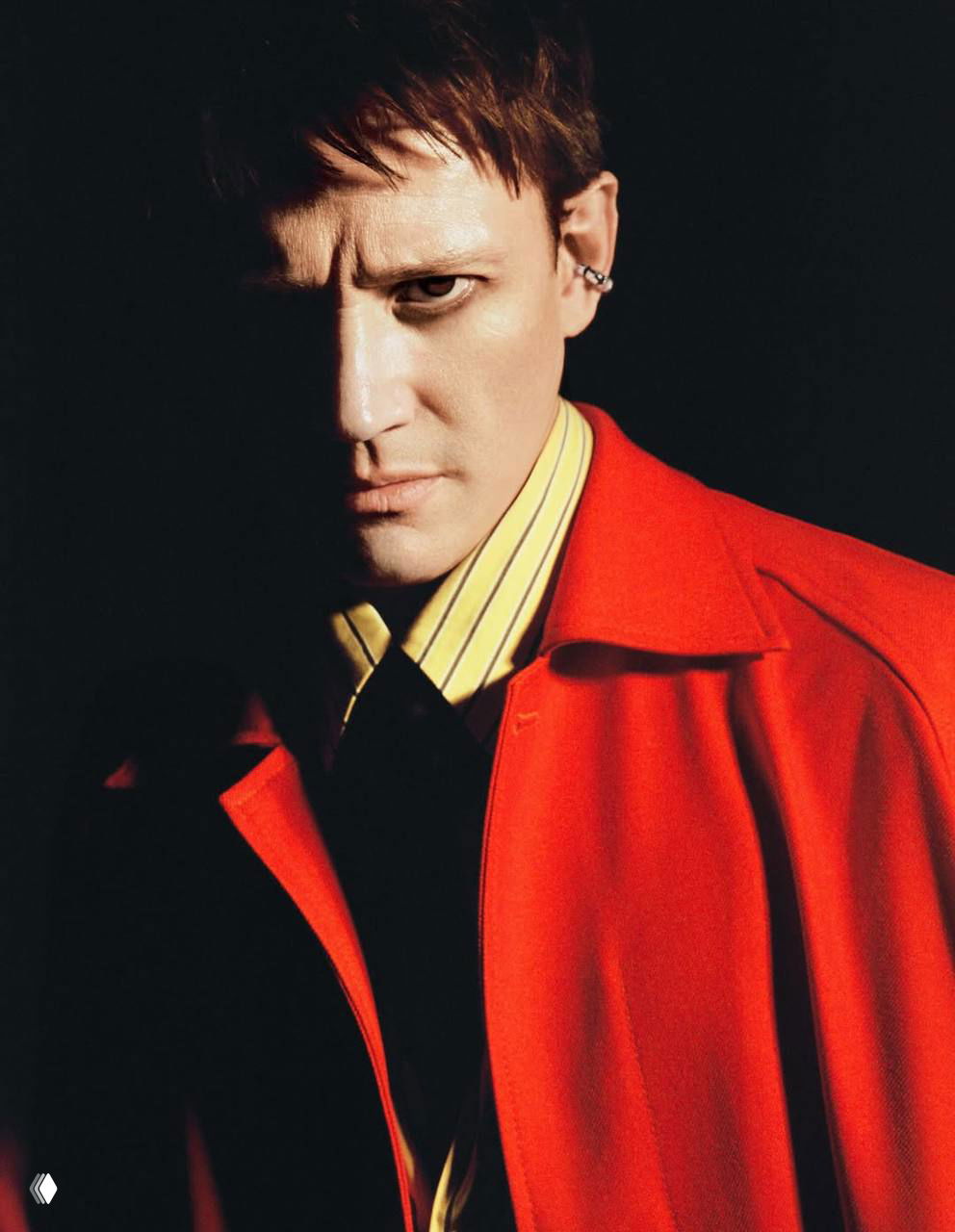 Контрастный портрет мужчины в ярком красном пальто, половина лица скрыта тенью, киношное освещение подчёркивает напряжение образа.