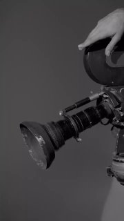 Крупный план объектива и части ретро-кинокамеры на тёмном фоне — деталь съёмочной сцены фотосессии для журнала.