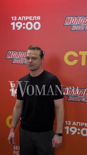 Гость на красной дорожке у баннера с логотипом и временем премьеры «Молодёжка. Новая смена», виден водяной знак Woman.ru.