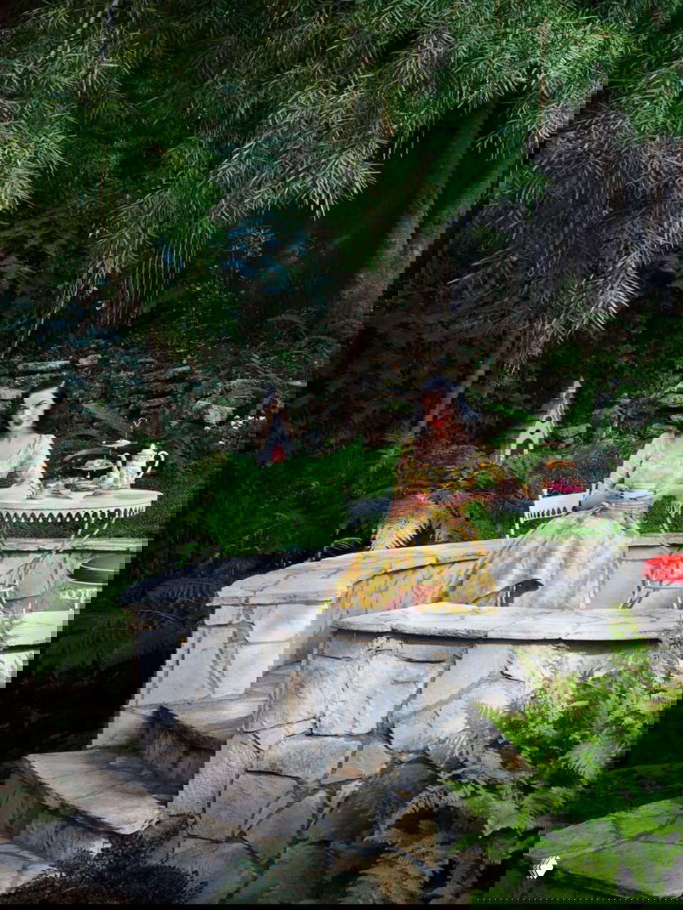 Дита в саду за столиком среди зелени и каменных ступеней — уголок с винтажной мебелью и романтическим садовым антуражем