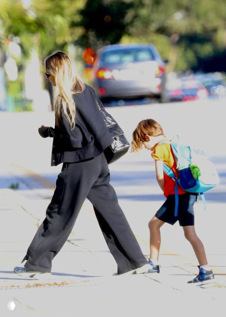 Кадр папарацци: Анна Курникова идёт по тротуару в чёрной спортивной одежде, рядом ребёнок в оранжевой футболке с рюкзаком.