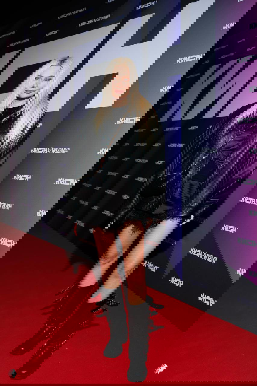 Молодая женщина в чёрной кожаной куртке и высоких ботинках позирует на ковровой дорожке у логотипа KION во время празднования юбилея онлайн‑кинотеатра в Театре на Цветном.