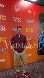 Гость на красной дорожке на фоне рекламного баннера сериала «Молодёжка. Новая смена»; на изображении виден логотип и водяной знак Woman.ru.