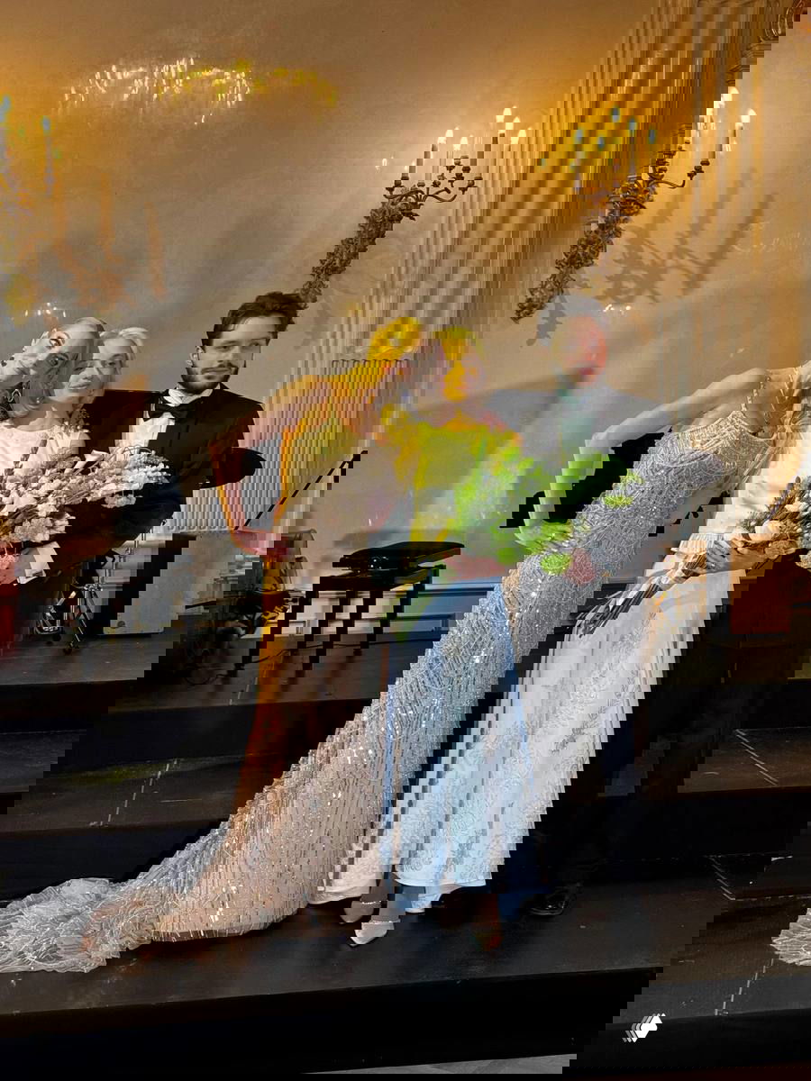 Анастасия Волочкова с дочерью Ариадной и зятем на праздничной сцене: нарядные платья, букет, вечерняя зала и люстры на заднем плане, семейный снимок после свадьбы.