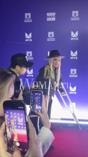 Ольга Бузова за кулисами с блестящими костылями на красной дорожке; фанаты снимают на телефоны, заметны баннеры и брендовые логотипы