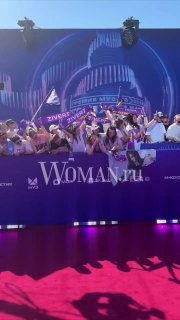 Поклонники на красной дорожке у баннера Woman.ru встречают певицу под громкие аплодисменты; видно сцену, фан-сектор и яркую ковровую дорожку на фоне.