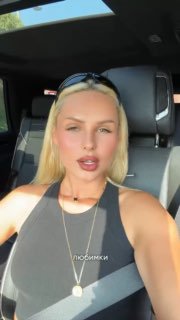 Крупный план певицы Ханна в автомобиле: блондинка в чёрной майке на солнечном свету, обращается к поклонникам из машины в Дубае.