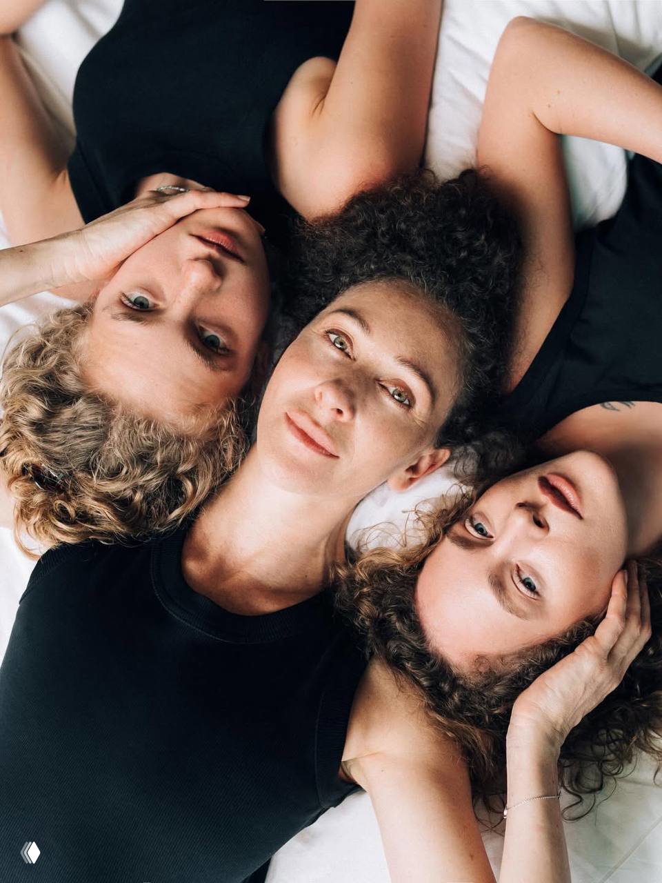 Три женщины — Ксения Раппопорт в центре и члены семьи рядом — лежат головами вместе на постели, портретная композиция архивного семейного фото.