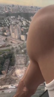 Крупный план оголённой руки и части бедра на фоне широкой городской панорамы с высоты; вертикальное видео, вид из окна небоскрёба.