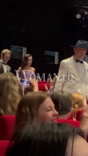 Интерьер кинозала и часть аудитории на премьере: зрители в красных креслах и люди в вечерних нарядах на фоне сцены.