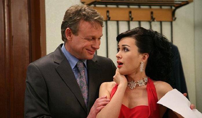 Кадр с официально одетыми персонажами в сцене светского мероприятия: женщина в вечернем платье и мужчина в костюме обмениваются репликами, эмоциональный момент.