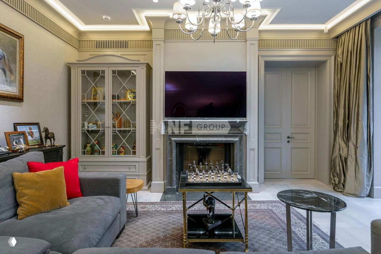 Гостиная с камином и большим телевизором над ним, мягкая мебель, стеклянные витрины и кофейный стол с шахматной доской в классическом интерьере.