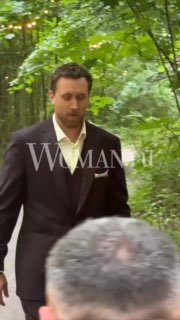 Мужчина в тёмном костюме идёт по аллее в зелёном парке; кадр с видимым водяным знаком «WOMAN.ru», похоже на момент со свадьбы.