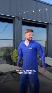 Мужчина в синей спортивной куртке стоит на открытой террасе у стеклянных дверей; на фото видно текст-наложение о страхе высоты и эмоциях после прыжка.