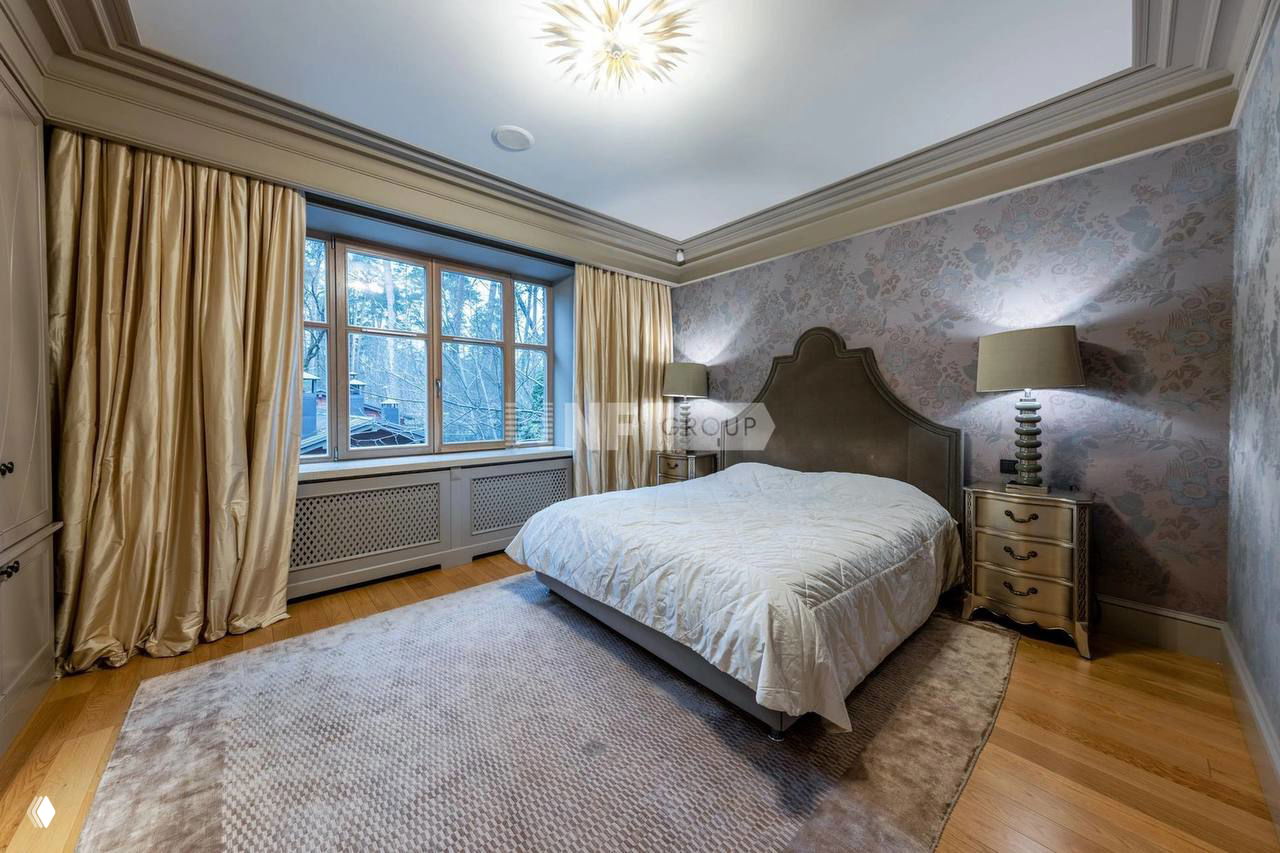 Спальня с широкой двуспальной кроватью, плотными шторами, мягким ковром и деревянным паркетом; спокойная нейтральная отделка стен и ночные лампы.