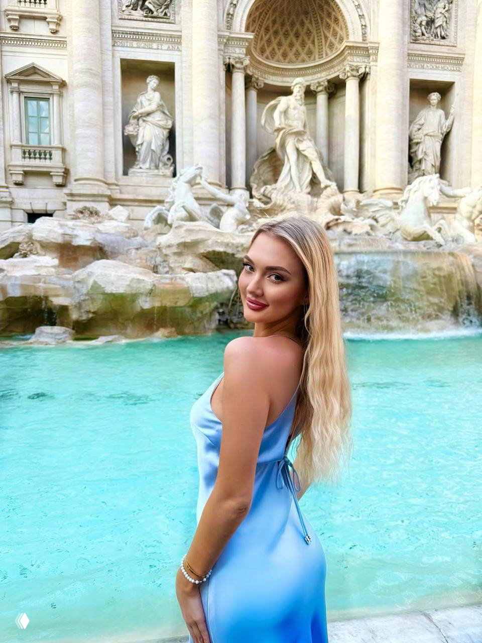 Портрет Ксении Гнединой на фоне знаменитого фонтана Треви в Риме: светло-голубое летнее платье, полупрофиль и туристический фон достопримечательности.
