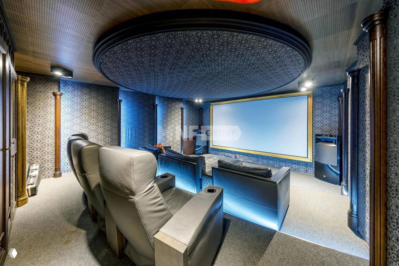 Домашний кинотеатр с рядом кожаных кресел-реклайнеров, большим экраном и декоративной потолочной конструкцией; затемнённая атмосфера для просмотра.