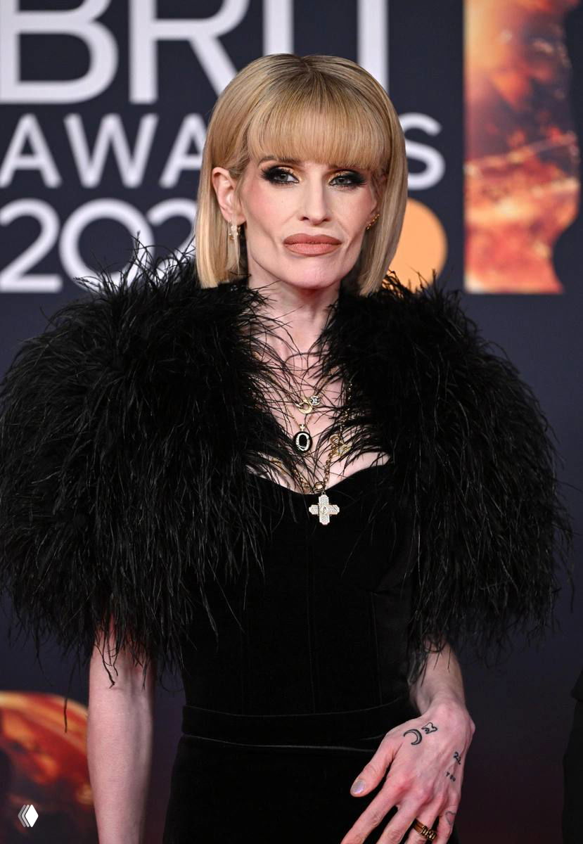 Крупный план Келли Осборн на Brit Awards 2026: бледное лицо, тонкие руки и выраженная худоба в чёрном платье на фоне логотипа мероприятия.