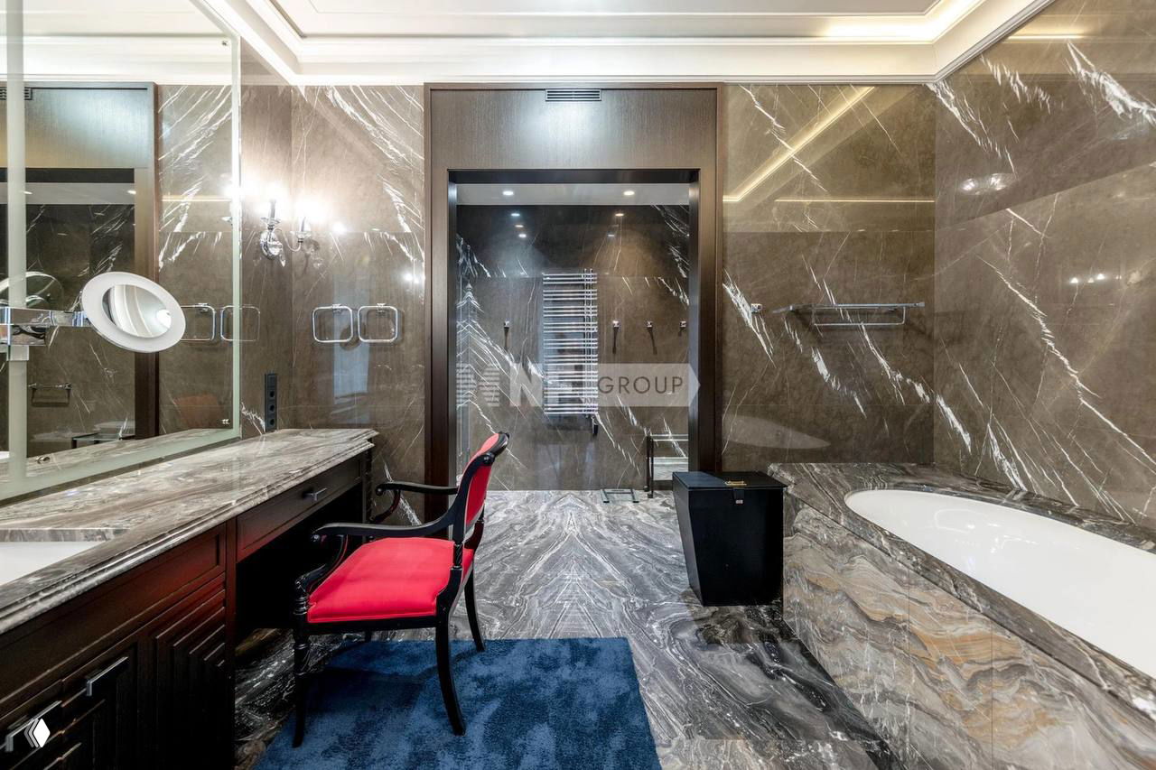 Ванная комната с богатой мраморной отделкой стен и пола, большой ванной и столешницей с зеркалом в элегантном классическом стиле интерьера.