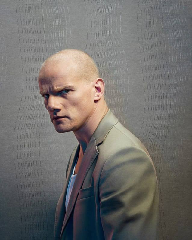 Студийный портрет мужчины в пиджаке с серьёзным выражением лица на нейтральном фоне; художественный кадр для журнала.