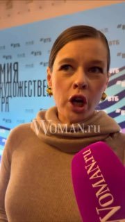 Крупный план: Екатерина Шпица даёт интервью на премии МХТ; в кадре микрофон с логотипом и водяной знак WOMAN.ru, видно выражение лица и макияж.