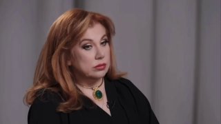 Портрет Марины Федункив в студии: серьёзный взгляд, тёмная одежда и зелёный кулон — кадр из интервью о позднем материнстве.