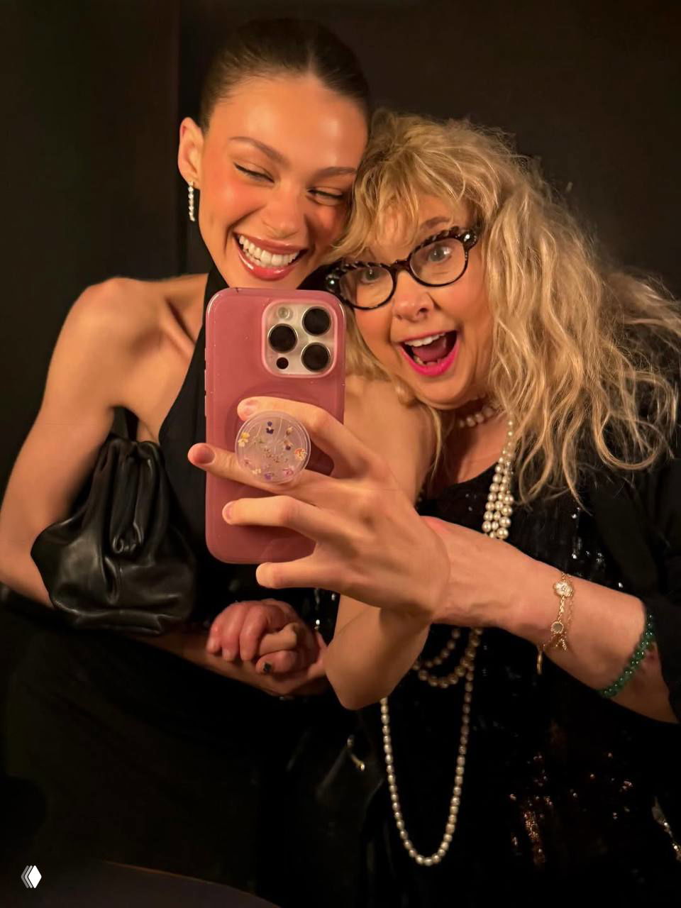 Никола Пельтц улыбается вместе с женщиной в вечернем туалете; селфи в зеркале с розовым чехлом iPhone и праздничными нарядами